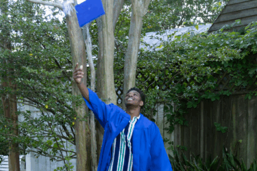 graduating student wearing a cap and gown and throwing cap in the air to celebrate class of 2025