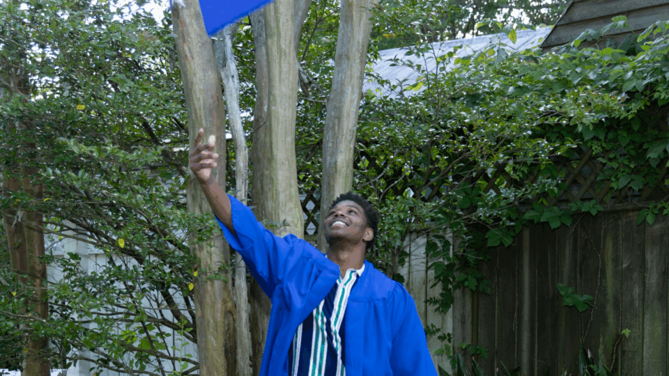 graduating student wearing a cap and gown and throwing cap in the air to celebrate class of 2025