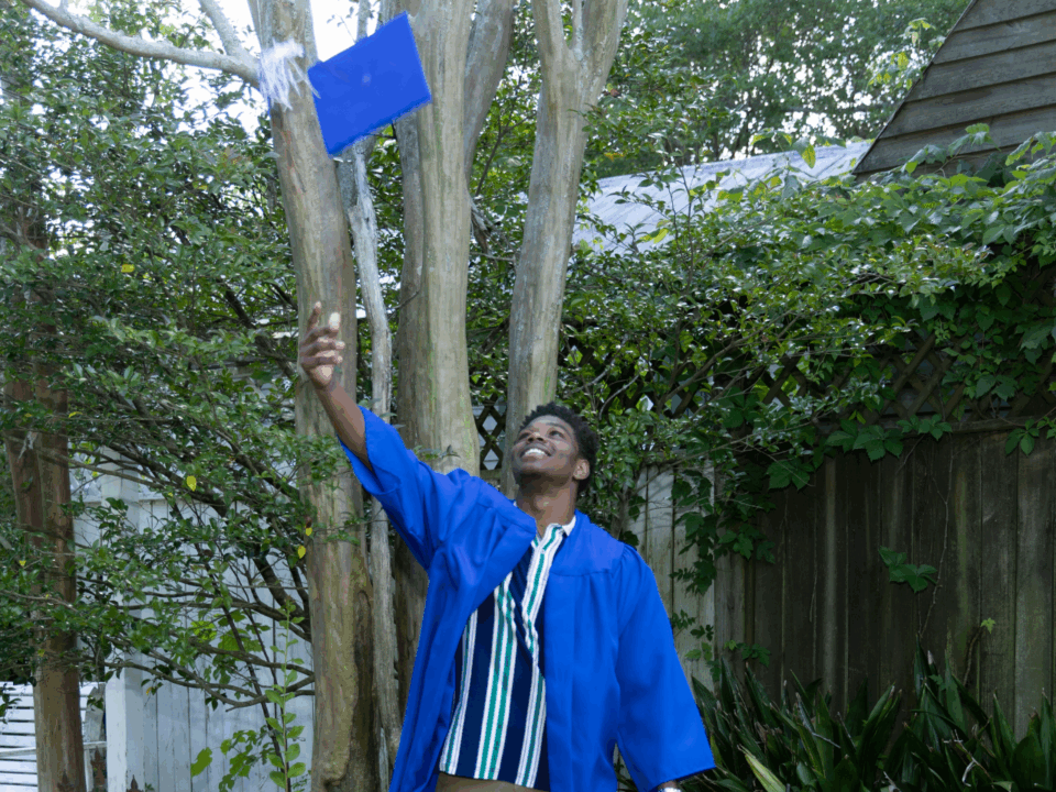 graduating student wearing a cap and gown and throwing cap in the air to celebrate class of 2025