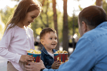 son and daughter holding popcorn with father at outdoor movies