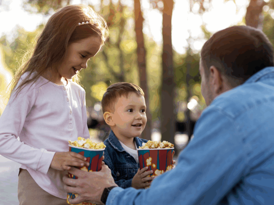 son and daughter holding popcorn with father at outdoor movies