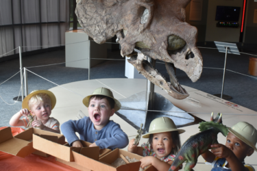Dino Day at LASM; four children standing in front of “Jason,” a 66-million-year-old Triceratops skull