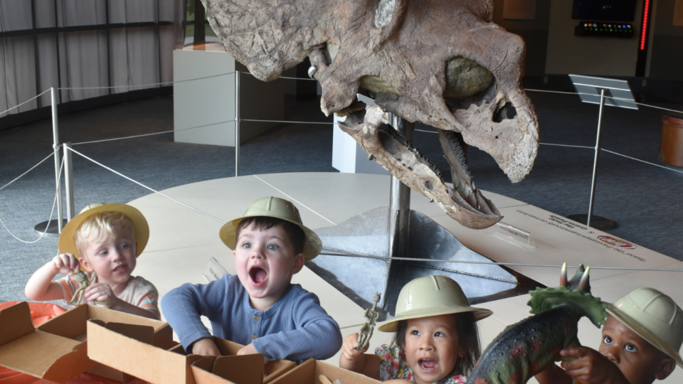 Dino Day at LASM; four children standing in front of “Jason,” a 66-million-year-old Triceratops skull