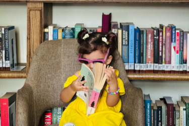 summer reading challenge; girl reading library book in library with sunglasses on