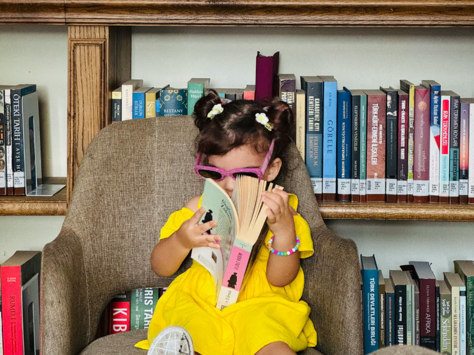 summer reading challenge; girl reading library book in library with sunglasses on